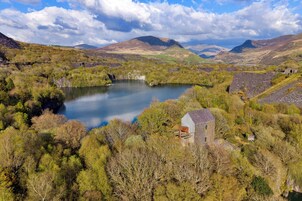 Paisagem rural com um lago, um pequeno edifício e colinas ao redor.