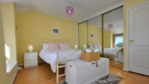 Quarto com cama, mesas de cabeceira, espelho e luminária no teto.