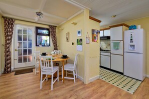 Cocina compacta con zona de comedor, piso de madera y refrigerador blanco.