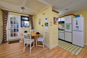 A compact kitchen with a dining area, wooden flooring, and a white refrigerator.