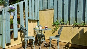 Um pátio com duas cadeiras de metal e uma pequena mesa, um cercado de madeira e um vaso com planta.