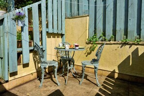 Eine Terrasse mit zwei Metallstühlen, einem kleinen Tisch, einem Holzzaun und einem Blumentopf.