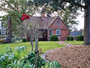 A brick house with a chimney, surrounded by a garden with a statue, a tree, and a pathway. - Charming Derbyshire Cottage (Ashbourne)