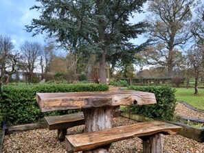 A rustic wooden picnic table with benches, set in a park with trees and a hedge in the background. - Charming Derbyshire Cottage (Ashbourne)