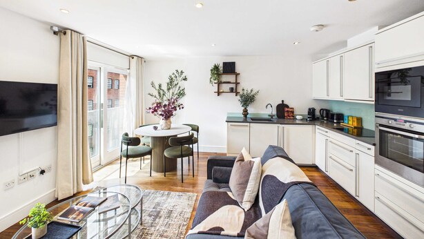 A modern apartment with a living room, dining area, and kitchen. There is a sofa, a dining table with chairs, and a kitchen counter with appliances. - Comfortable 1BR Apartment in Westminster (Greater London)