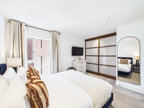 A modern hotel room with a large bed, a TV, a wardrobe, and a sliding door to a balcony. - Comfortable 1BR Apartment in Westminster (Greater London)