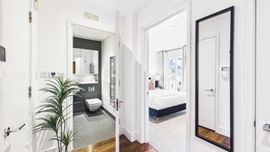 A modern hotel room with a large bed, a bathroom with a toilet and sink, and a hallway leading to another room. - Comfortable 1BR Apartment in Westminster (Greater London)