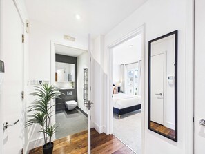 Ein modernes Hotelzimmer mit einem großen Bett, einem Badezimmer mit Toilette und Waschbecken sowie einem Flur, der in ein weiteres Zimmer führt.