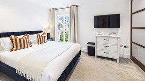 A hotel room with a bed, a television, a desk, and a window with curtains. - Comfortable 1BR Apartment in Westminster (Greater London)