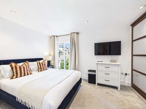 Ein Hotelzimmer mit einem Bett, einem Fernseher, einem Schreibtisch und einem fensterbepflanzten Fenster.