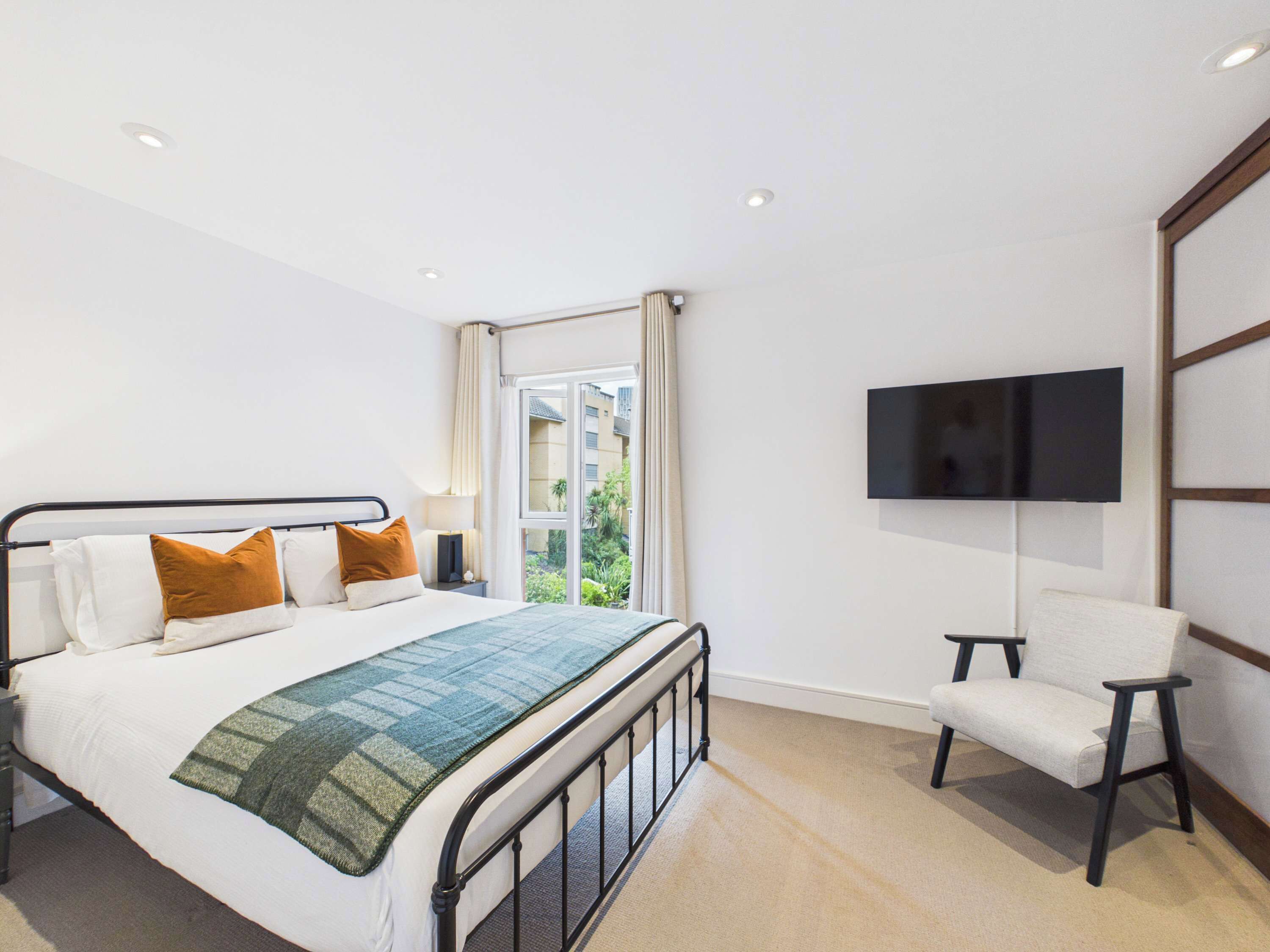 Habitación de hotel con cama, televisor montado en la pared y ventana con vistas a zonas verdes.