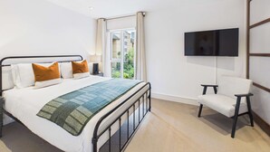 Ein Hotelzimmer mit Bett, einem an der Wand befestigten Fernseher und einem Fenster mit Blick ins Grüne.