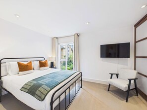 Quarto de hotel com cama, TV fixada na parede e janela com vista para o verde.