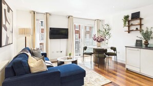 Ein modernes Wohnzimmer mit einem blauen Sofa, einem Esstisch mit Stühlen und einer Küchenzeile mit einem weißen Schrank.