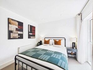 Quarto moderno com cama, abajures, mesa de cabeceira e arte abstrata na parede.