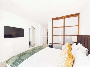 A hotel room with a bed, a television mounted on the wall, a large mirror, and a sliding door. - Westminster Spacious Apartment with Balcony (Greater London)