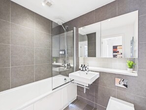 A modern bathroom with a bathtub, a sink, and a large mirror. - Westminster Spacious Apartment with Balcony (Greater London)