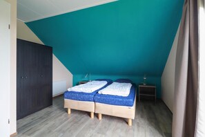 A bedroom with a sloped ceiling, two beds, a wardrobe, bedside lamps, and a radiator. - Comfortable 4-person Bungalow With Jetty (Makkum)