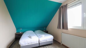 Ein Zimmer mit Bett, Nachttisch, Lampe und einem fensterbepflegten Fenster.