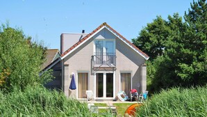 Ein zweistöckiges Haus mit Balkon, Eingangstür und einer kleinen Veranda mit Gartenmöbeln.