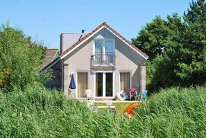 A two-story house with a balcony, a front door, and a small porch area with outdoor furniture. - Comfortable 4-person Bungalow With Jetty (Makkum)