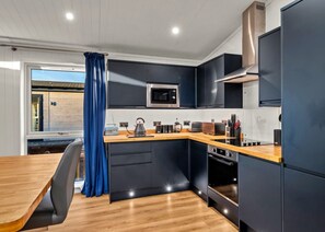A modern kitchen with dark cabinetry, a microwave, a kettle, and a wooden countertop. - Peaceful Lochside Retreat for 4 (Perth)