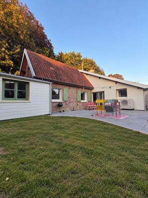 A two-story house with a red-tiled roof, a small attached garage, and a front yard with a lawn and a patio area. - Maison la Rosie - Air conditioning on the patio and in the garage (Blendecques)