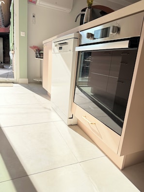 A kitchen with a built-in oven and dishwasher, a tiled floor, and a view of the outside. - Maison la Rosie - Air conditioning on the patio and in the garage (Blendecques)