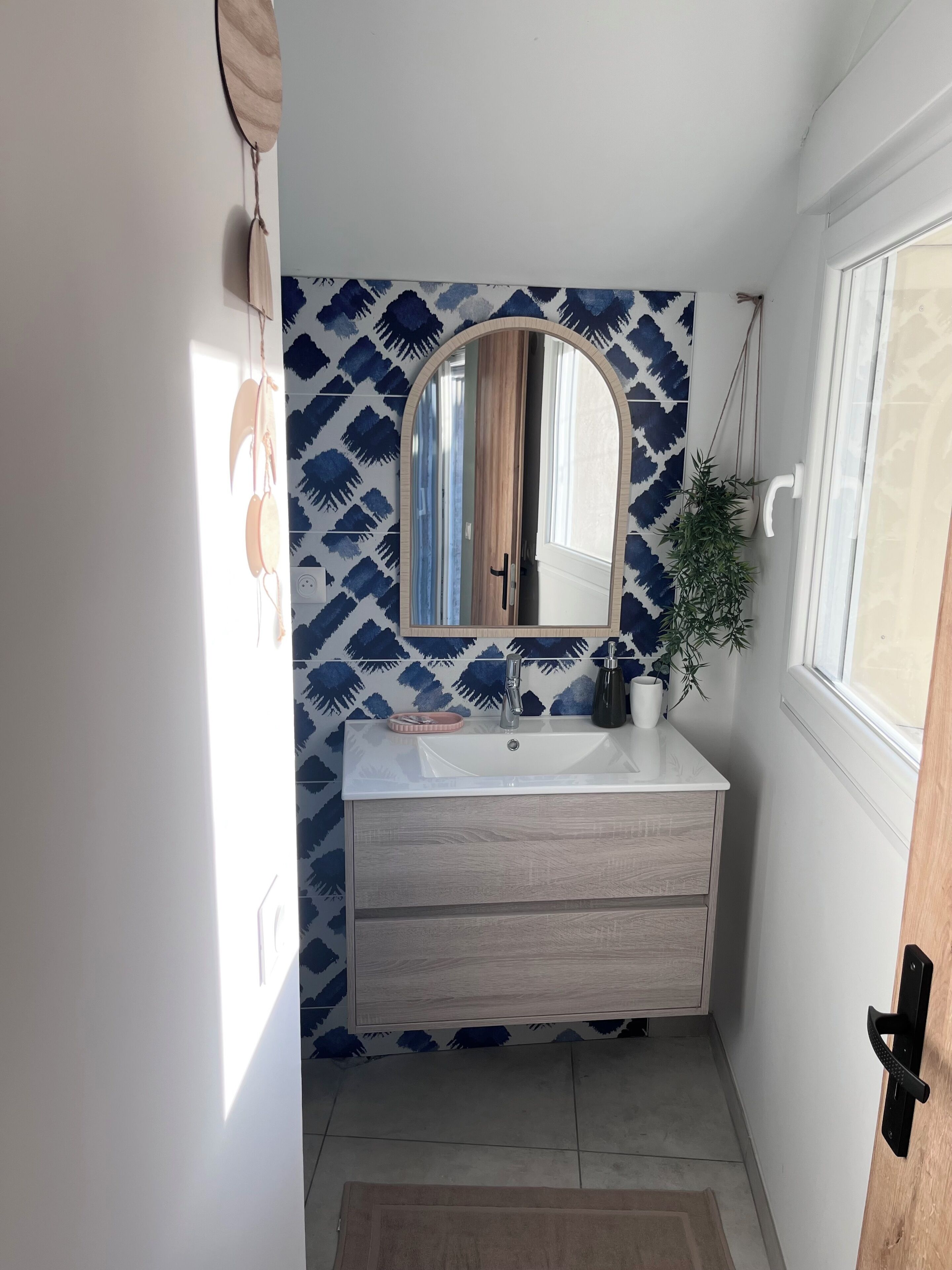 A bathroom with a white sink, a mirror, and a patterned wall.
