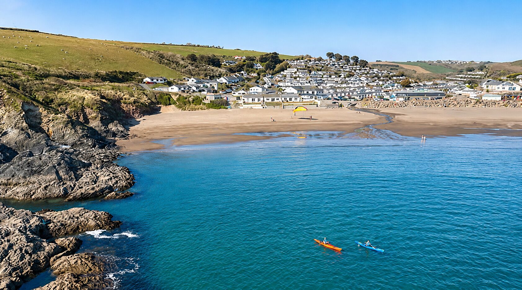 A coastal town with a beach, rocky shoreline, and clear blue waters.