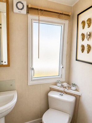 Ein Badezimmer mit Toilette, Waschbecken, einem Fenster mit Blick und einem gerahmten Bild an der Wand.