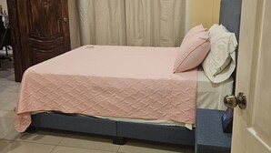 Une chambre à coucher comprenant un lit, un ventilateur de plafond, une porte et un climatiseur fixé au mur.