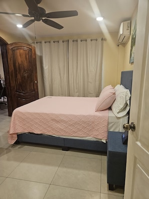 A bedroom with a bed, a ceiling fan, a door, and a wall-mounted air conditioner.