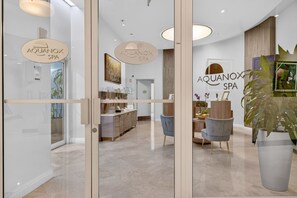 Interior moderno de spa, com portas de vidro, um balcão de recepção, área de refeições e uma grande planta em vaso.