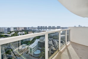 Un edificio alto con balcón de cristal que domina un paisaje urbano con varios edificios y un río.