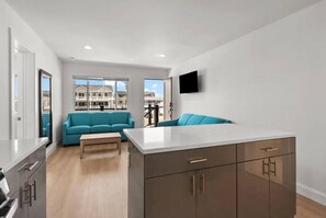 A modern apartment with a kitchen, a living area with a sofa, and a balcony with a view of houses.