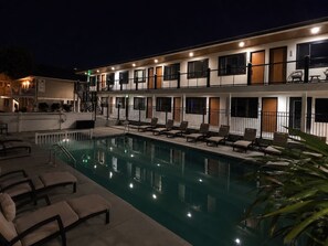 A hotel with a swimming pool, multiple balconies, and lounge chairs.