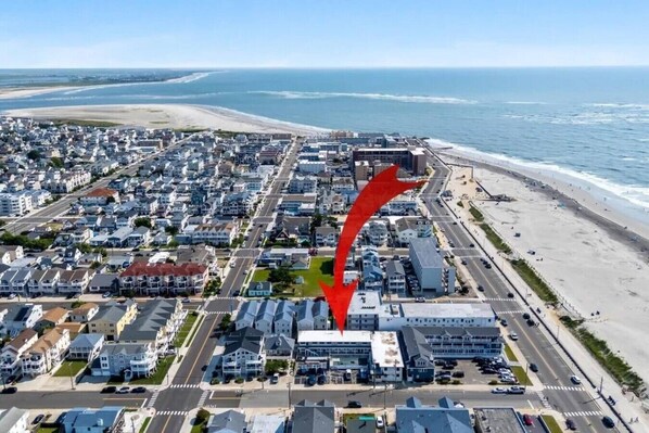An aerial view of a coastal residential area with a beach, houses, and a road.
