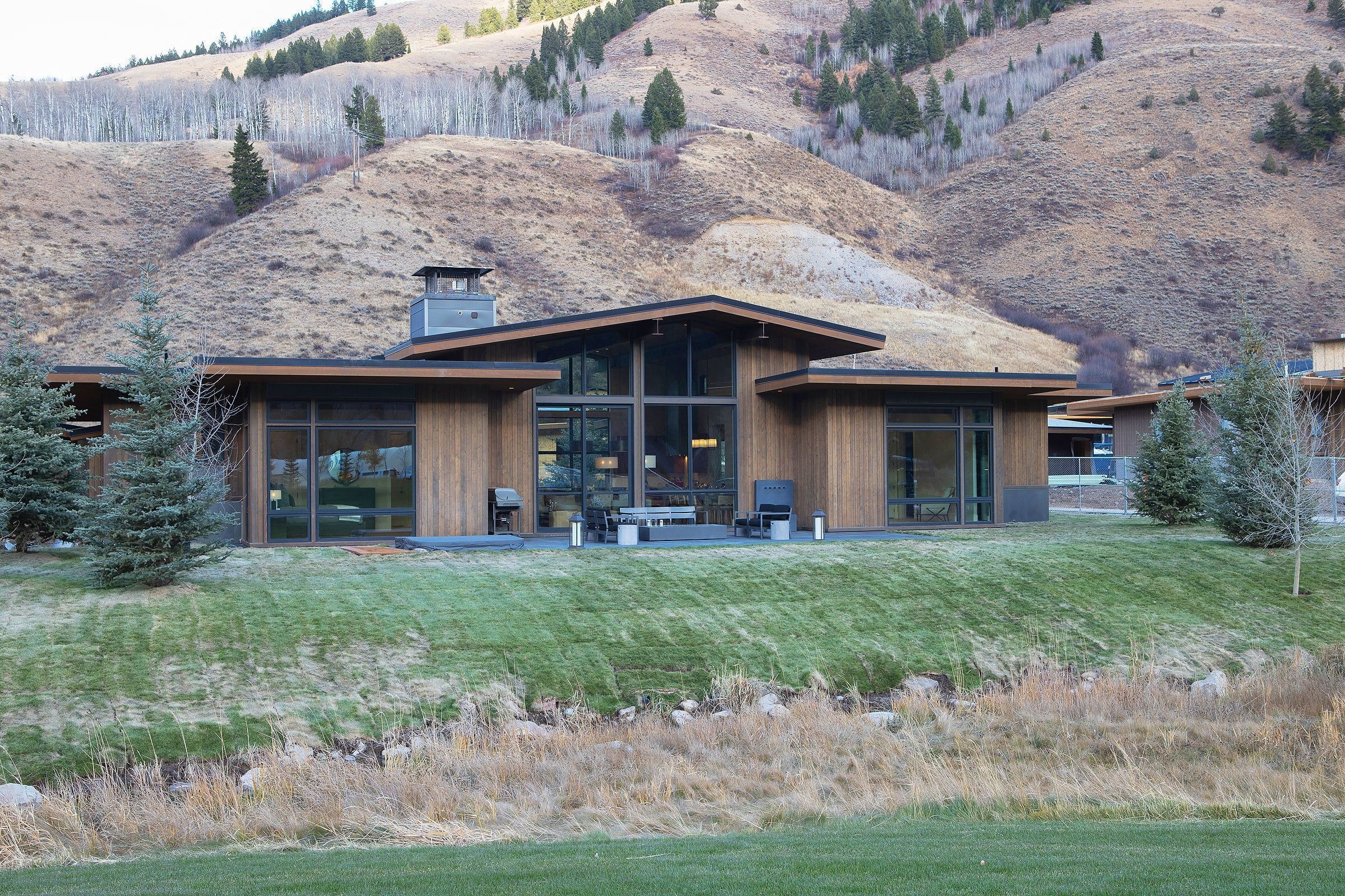 A modern house with large windows, a covered patio, and a view of a hilly landscape.