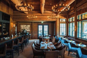 Un restaurant aménagé dans un style de chalet en rondins, avec des murs en bois, un bar et une salle à manger dotée de chaises et de tables en cuir.