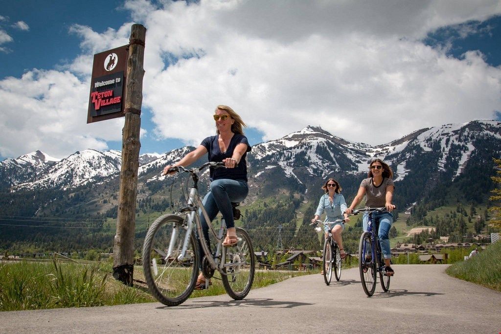 Trois personnes font du vélo sur un chemin, et un panneau indique : « Bienvenue à ZETON VILLAGE ».