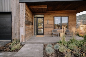 A modern building with a wooden exterior, a glass door, and a seating area with chairs and plants. - Spacious 3BR Meadow Cabin | Views, Patio & Hot Tub (Jackson)