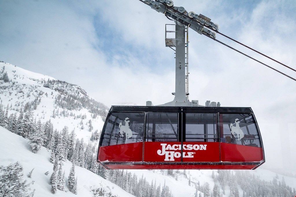 A cable car with 'Jackson Hole' branding, suspended above a snowy mountain landscape.