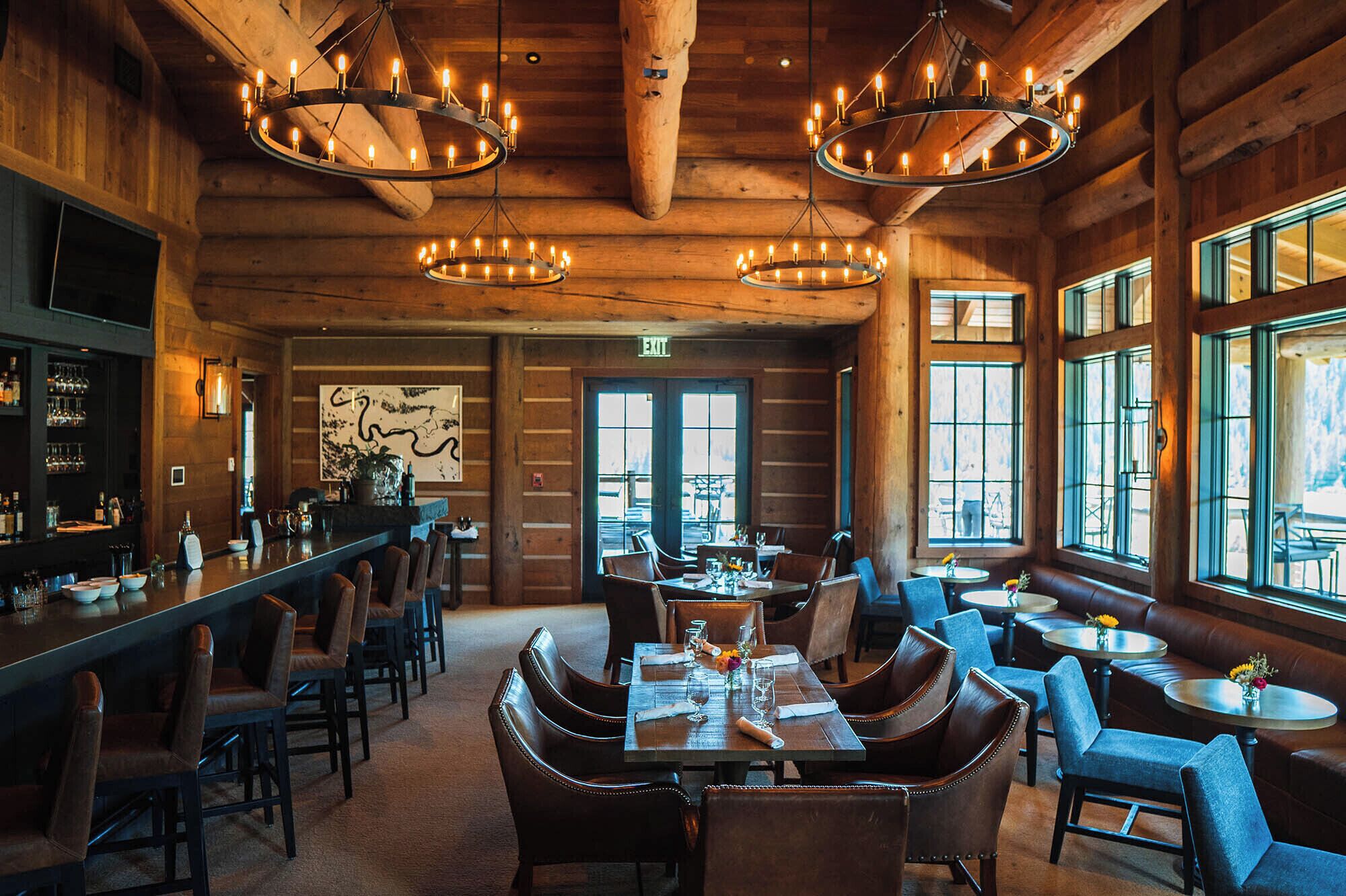 A restaurant with wooden interiors, multiple dining tables, and a bar area.