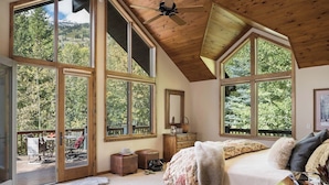 Un'ampia camera da letto con ampie finestre, soffitto in legno e vista sull'esterno.