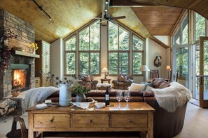 A cozy living room with a fireplace, large windows, and comfortable seating. - Mountain Home w/ Private Hot Tub & Garage (Jackson Hole)