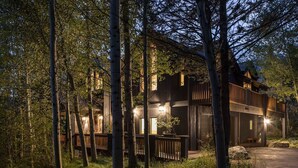 Una moderna baita di legno immersa tra gli alberi, con una terrazza e una panchina.