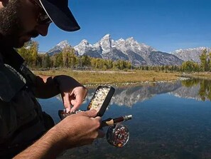 A person holding a fishing rod over a calm lake with mountains in the background. - Mountain Home w/ Private Hot Tub & Garage (Jackson Hole)
