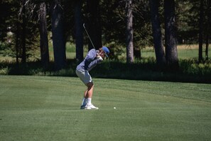 Eine Person spielt Golf auf einem gepflegten Rasen, im Hintergrund Bäume.