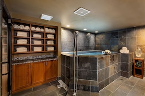 A modern bathroom with a built-in shower, a wooden towel rack, and a stone wall. - Luxury Private Mountain Home w/ Hot Tub (Jackson Hole)